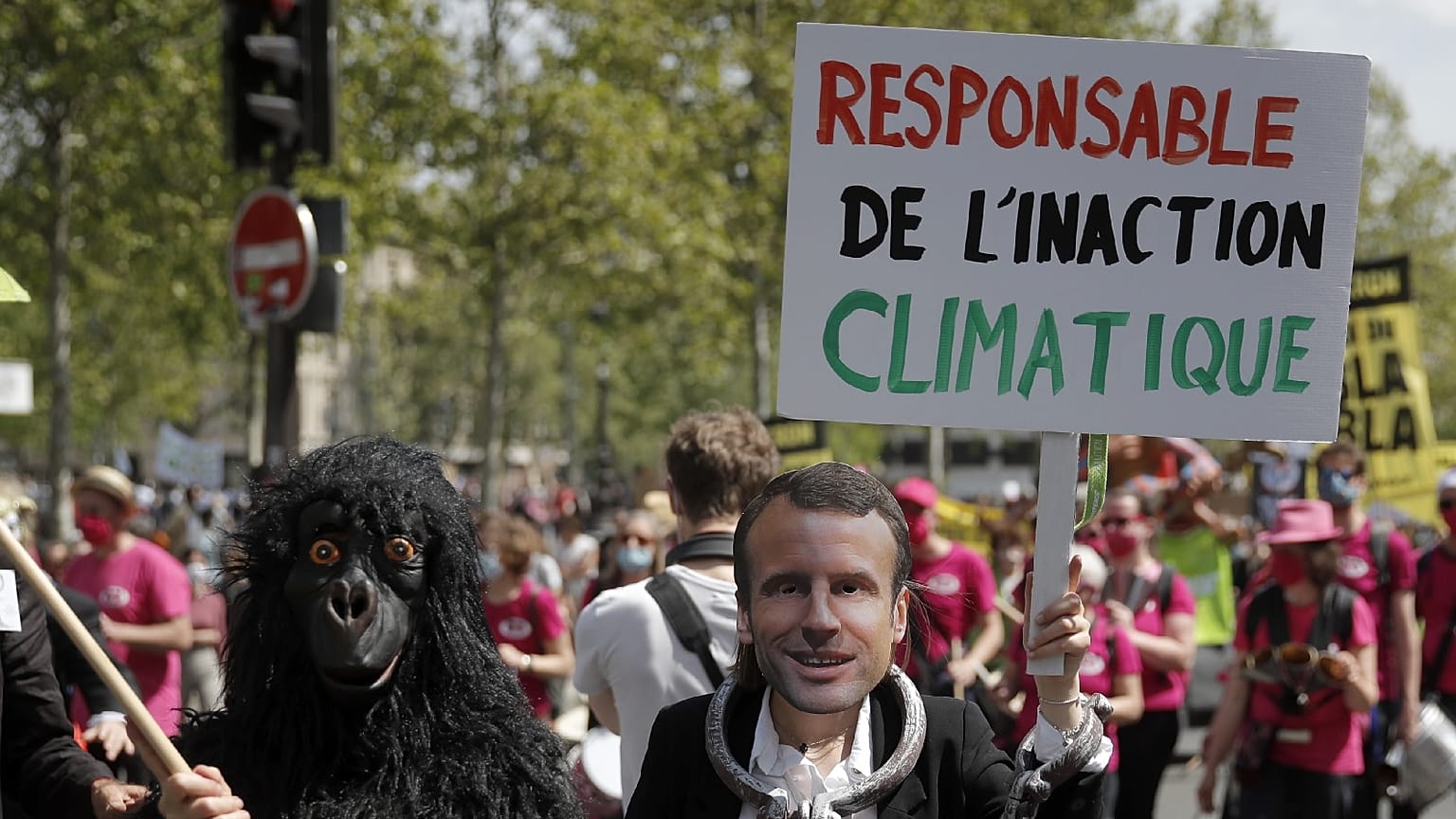 A protester wearing a mask depicting French President Emmanuel Macron holds a bord reading « Liable for climate inaction » during a rally in Paris, May 9, 2021.