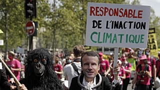 A protester wearing a mask depicting French President Emmanuel Macron holds a bord reading « Liable for climate inaction » during a rally in Paris, May 9, 2021.