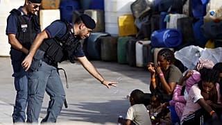 A police officer plays with a migrant child blowing soap bubbles in the port of the Sicilian island of Lampedusa, southern Italy, Monday, Sept. 18, 2023.