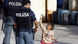 Agente da polícia olha para criança a brincar com bolas de sabão no porto de Lampedusa, Itália