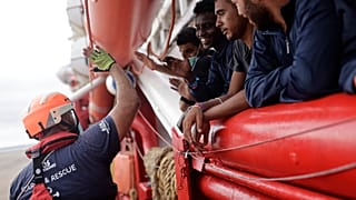 Un voluntario de SOS Mediterranee choca los cinco con unos inmigrantes que se acercan a las costas italianas, el 4 de septiembre de 2022 frente a Taranto, en el sur de Italia.
