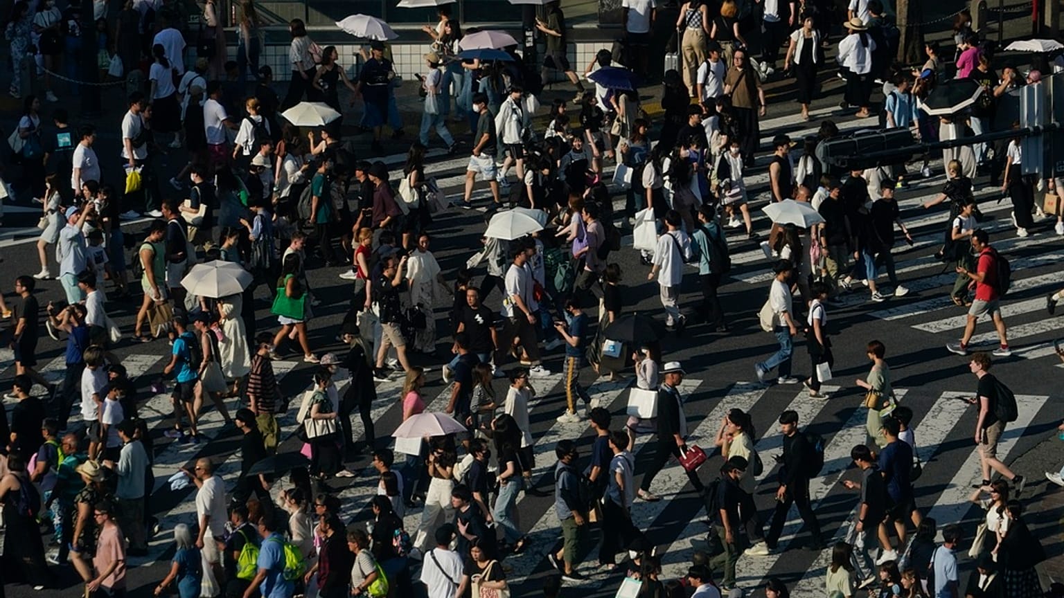 People carry umbrellas to shield themselves from the sun as they walk across an intersection Monday, July 17, 2023, in Tokyo. 
