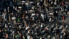 People carry umbrellas to shield themselves from the sun as they walk across an intersection Monday, July 17, 2023, in Tokyo. 