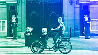 Un ciclista monta en una bicicleta de carga con niños delante de Los Guardias Reales de la Vida en el Castillo de Amalienborg en Copenhague, junio de 2023.