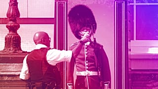 A police officer gives water to a British soldier wearing a traditional bearskin hat on guard duty outside Buckingham Palace, July 2022