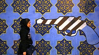 DATEI - Eine iranische Frau geht am Samstag, 2\. November 2013, in Teheran, Iran, an einem gegen die USA gerichteten Wandgemälde vorbei, das an die Wand der ehemaligen US-Botschaft gemalt wurde.
