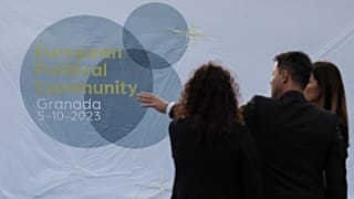 People stand in front of a logo of the European Political Summit, on the eve of the European Political Community summit in Granada, southern Spain on October 4, 2023.