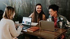 Three people share a joke while on their laptops.