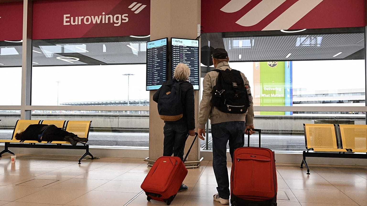 Reisende vor einem Bildschirm mit Flugdaten am Flughafen Köln-Bonn, Deutschland, April 2023.