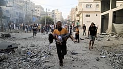A Palestinian carrying a child runs following an Israeli strike in the southern Gaza Strip on Saturday as fighting between Israel and Hamas continues for an eighth day