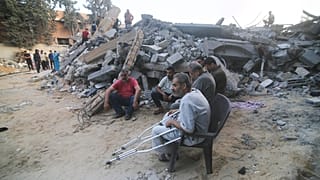 Palestinos sentados junto al edificio destruido en un ataque aéreo israelí en Rafah, Franja de Gaza, sábado 14 de octubre de 2023.