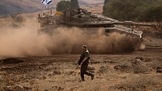 Un soldat israélien marche devant un char en mouvement surmonté d'un drapeau israélien dans une zone de transit près de la frontière israélienne avec le Liban, 15 octobre 2023