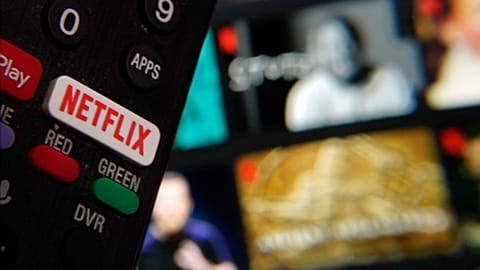 The Netflix button on a television remote control is juxtaposed with a Netflix web page, in February 2023.