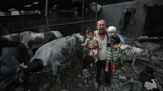 A man holds wounded children near livestock animals around the heavily damaged buildings after Israeli attacks at Nuseirat Refugee Camp on Sunday