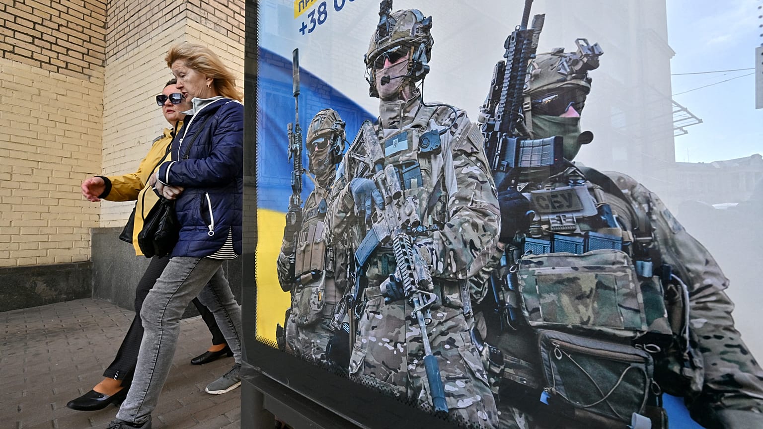 Pedestrians walk past a poster depicting Ukrainian servicemen and a slogan which reads "Bring the victory soon" in Kyiv, on 31 October