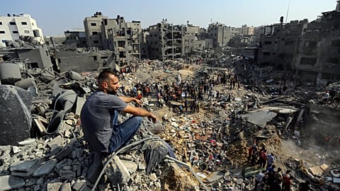 A man sits on the rubble as others wander among debris of buildings that were targeted by Israeli airstrikes in Jabaliya refugee camp, northern Gaza Strip, Wednesday, 1/11/23.