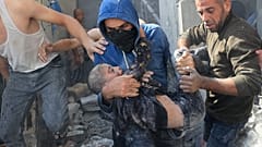 فلسطيني يحمل طفلا من تحت أنقاض مبنى مدمر في أعقاب غارة جوية إسرائيلية