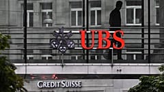 n employee of multinational investment bank UBS walks past a sign of Swiss giant banking UBS above a sign of Credit Suisse in Zurich on August 31, 2023.