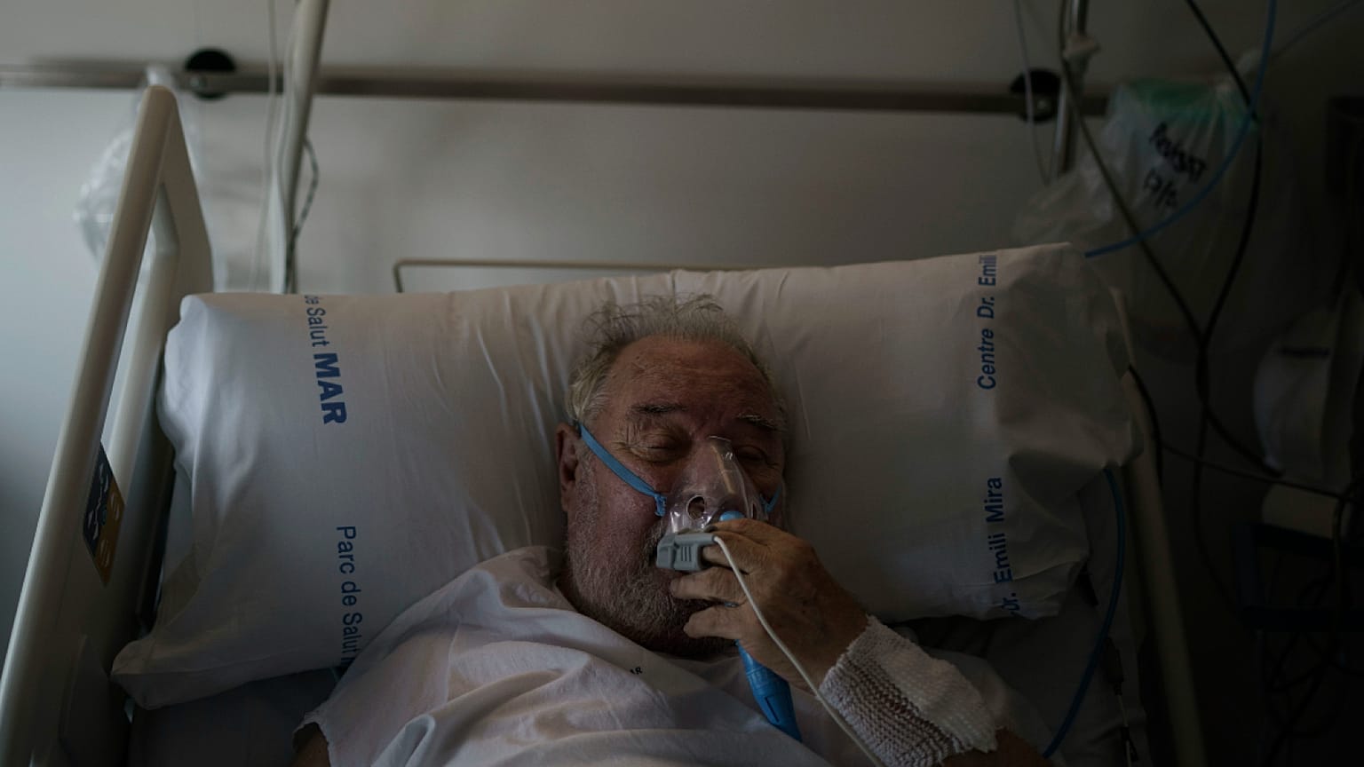 A COVID-19 patient adjusts his oxygen mask as he receives treatment in the Hospital del Mar in Barcelona, Spain, 2021.