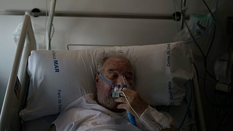 A COVID-19 patient adjusts his oxygen mask as he receives treatment in the Hospital del Mar in Barcelona, Spain, 2021.