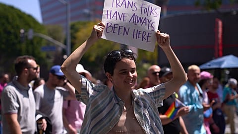 An LGBTQ+ activist holds a sign reading 'Trans Folks Have Always Been Here' in April