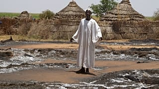 قروي سوداني من قرية أم هشاب، في ولاية شمال دارفور السودانية يقف أمام كوخه المحترق (أرشيف). 2004/08/29