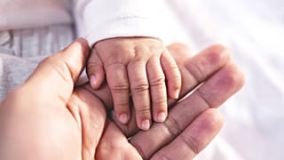 Parent holding their baby's hand