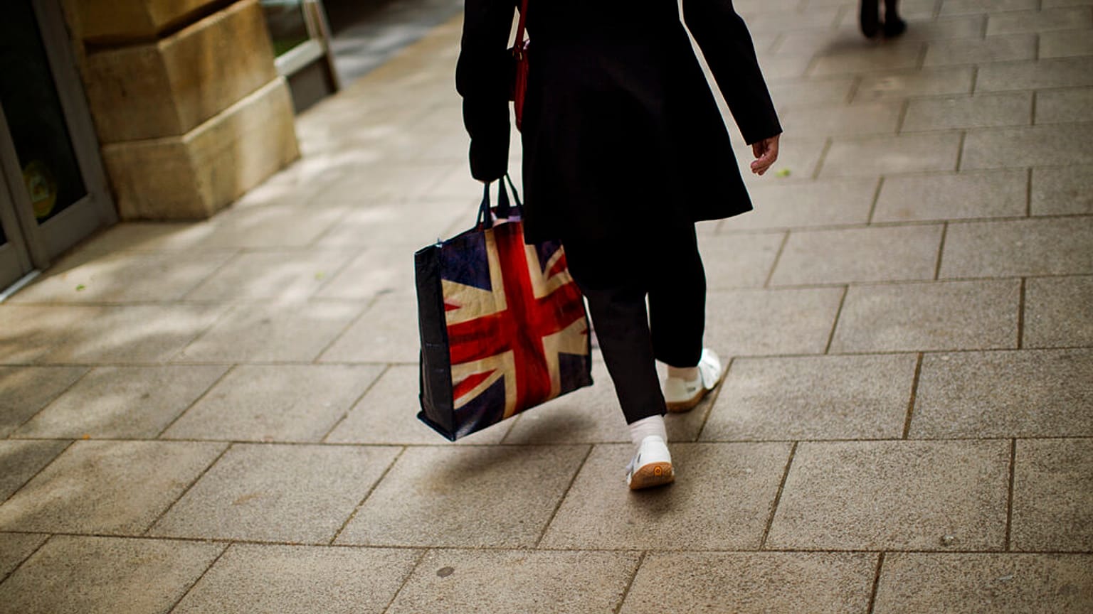 In this Tuesday, July 5, 2016 photo, a woman carrying a bag decorated with a Great Britain's union flag, walks a long a street in downtown Peterborough, East of England.