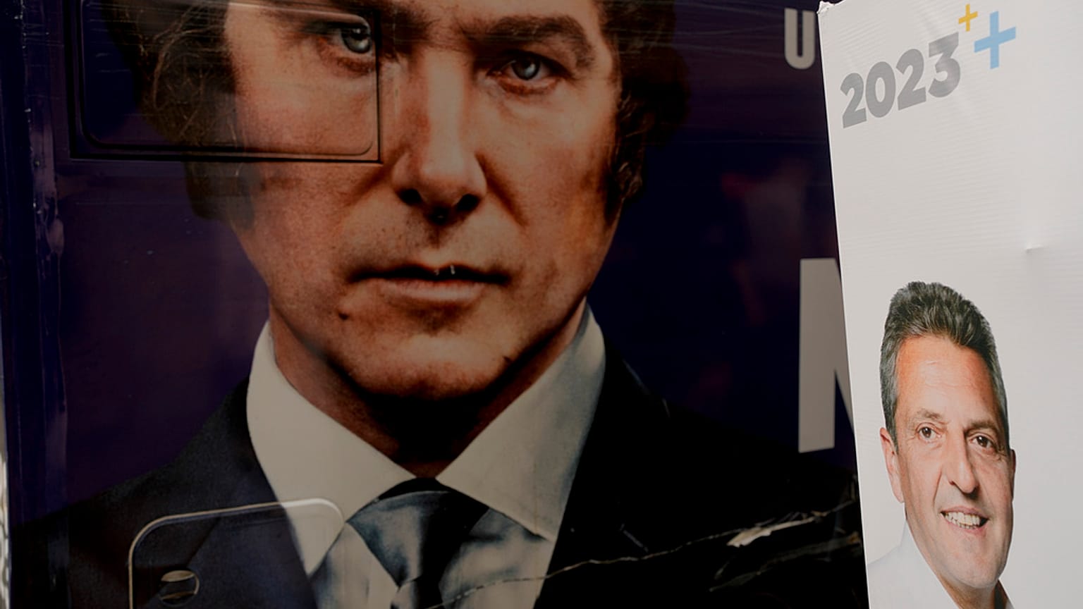 The image of presidential hopeful Javier Milei fills the side of a bus carrying his supporters, parked by a wall where a sign promotes his rival Sergio Massa, in Buenos Aires