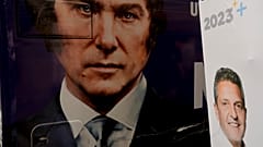 The image of presidential hopeful Javier Milei fills the side of a bus carrying his supporters, parked by a wall where a sign promotes his rival Sergio Massa, in Buenos Aires
