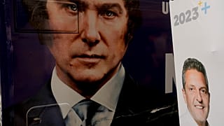 The image of presidential hopeful Javier Milei fills the side of a bus carrying his supporters, parked by a wall where a sign promotes his rival Sergio Massa, in Buenos Aires
