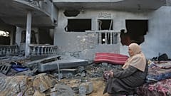 Eine palästinensische Frau sitzt am Montag, 20. November 2023, in Rafah neben Häusern, die durch die israelische Bombardierung des Gazastreifens zerstört wurden. 