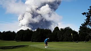 A man plays gold in Hawaii in 2018 as a huge ash plume rises behind him.