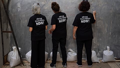 People write on an installation simulating a tunnel in Gaza in an act of solidarity with hostages believed to be held underground by Hamas and calling for their return, in Tel
