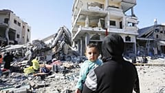 A child is seen in a woman's arms as displaced Palestinians, taking shelter in hospitals and schools, walk amid destruction as a result of Israeli attacks