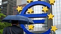 A man shelters from the rain under an umbrella as he walks past the Euro currency sign in front of the former European Central Bank (ECB) building in Frankfurt am Main, wester