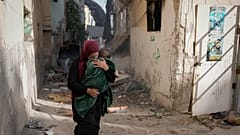امرأة فلسطينية تحمل طفلًا وتهرب في أحد شوارع مخيم جنين بعد اجتياحه من قبل الجيش الإسرائيلي