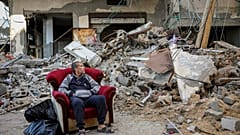 A Palestinian man sits in an armchair outside a destroyed building in Gaza City