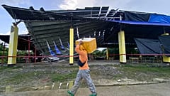 A fish vendor passes by a partially collapsed multipurpose covered court in Tagbina town, Agusan del Sur, southern Philippines on Sunday Dec. 3, 2023.