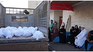 فلسطينيون يجلسون بالقرب من شاحنة مكدسة بالجثث أمام مستشفى الأقصى في غزة