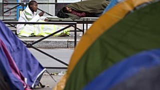 A man smokes near tents during the evacuation of a makeshift camp on June 16, 2016 in Paris.
