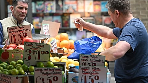 A customer pays for his fruit and vegetables with a ten pound sterling note, at a trader's market stall in London on May 12, 2022. Britain's economy shrank in March on fallout