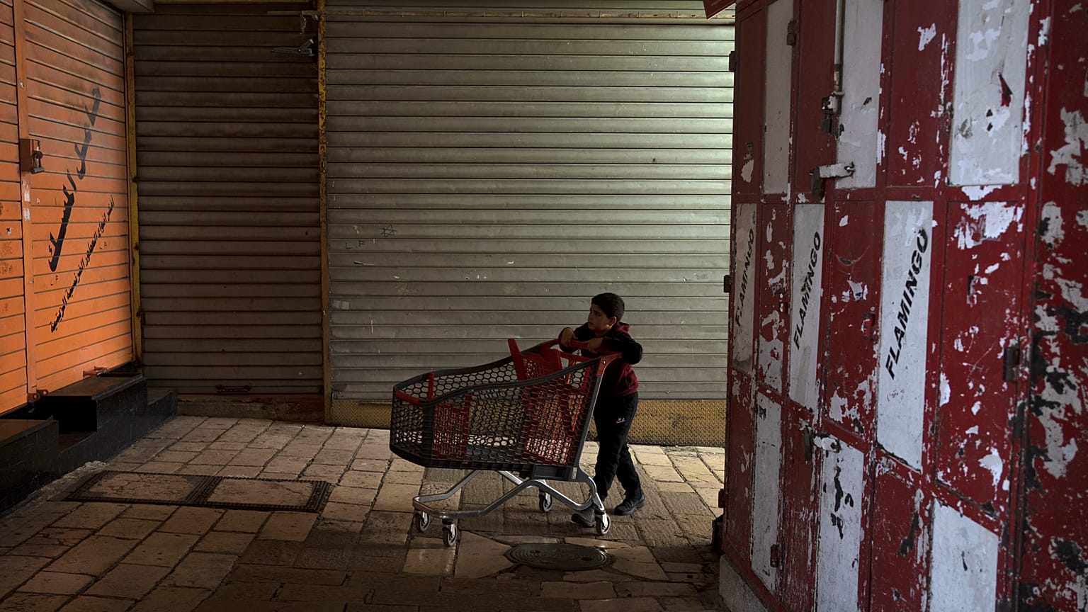 طفل فلسطيني يدفع عربة تسوق فارغة في أحد زقاق مدينة القدس