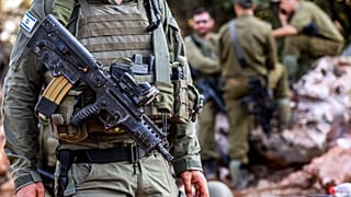 An Israeli army soldier - not one of the accused - stands with an assault rifle hanging across his chest 