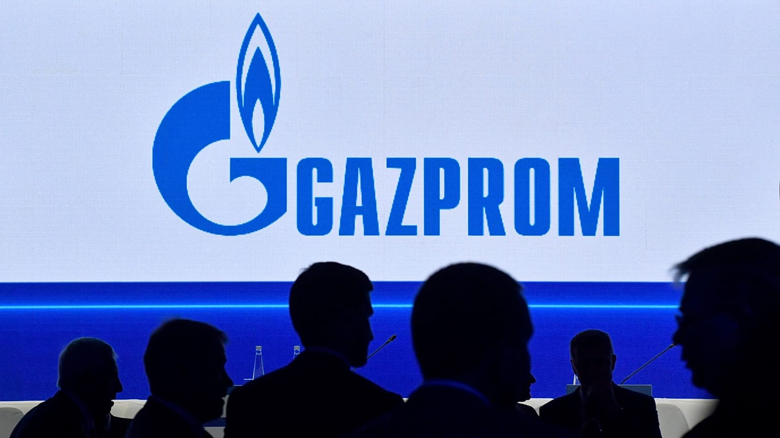 Participants walk in front of a large screen displaying the logo of Russia's energy giant Gazprom during the St. Petersburg International Gas Forum (SPIGF) in Saint Petersburg