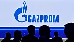 Participants walk in front of a large screen displaying the logo of Russia's energy giant Gazprom during the St. Petersburg International Gas Forum (SPIGF) in Saint Petersburg