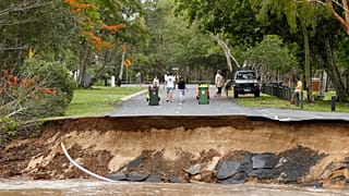 Stranded residents stand on a road, a large section of which has washed away, in the suburb of Holloways Beach in Cairns, Australia, Monday, Dec. 18, 2023.