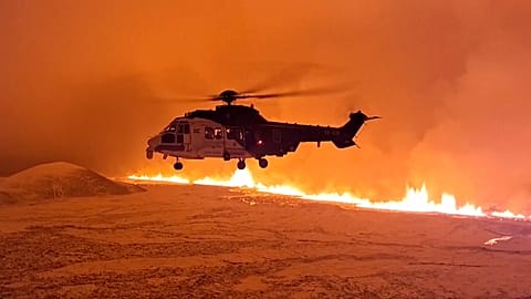 An Icelandic Coast Guard helicopter flies near magma running on a hill near Grindavik on Iceland's Reykjanes Peninsula.