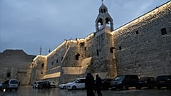أشخاص يسيرون بجوار كنيسة المهد في مدينة بيت لحم بالضفة الغربية، الجمعة 23 ديسمبر 2023