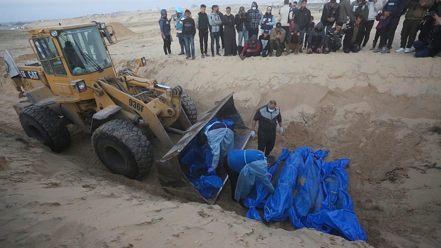 Un bulldozer scarica i corpi dei palestinesi uccisi nel nord della Striscia di Gaza e consegnati dall'esercito israeliano durante un funerale di massa a Rafah, il 26/12/2023